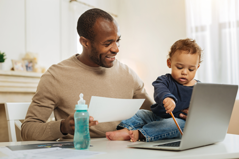 smiling father sitting with a toddler playing on a laptop