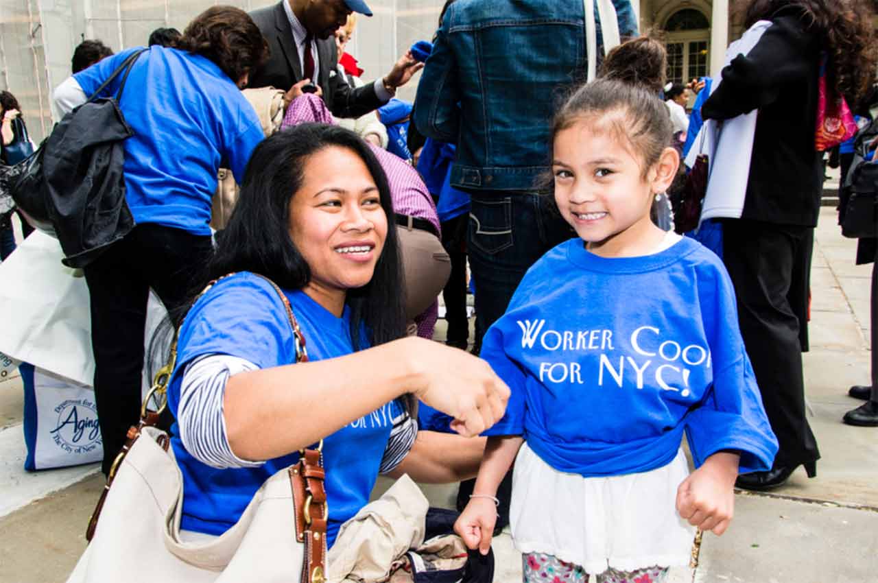 woman with child wearing "worker coop for NYC" t shirt at a protest