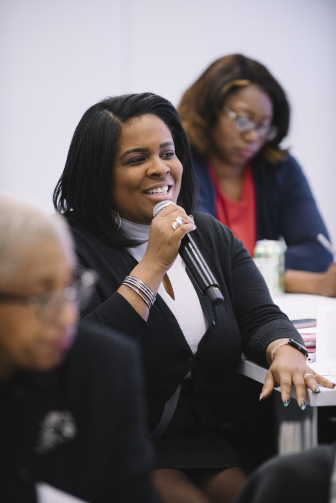 smiling woman holding a microphone and speaking while at a table